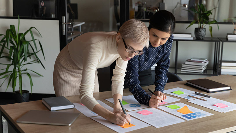 Decorative photo showing two female coworkers reviewing reports in a conference room