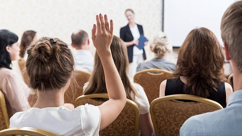 female professional with raised hand asks question in meeting female professional with raised hand asks question in meeting